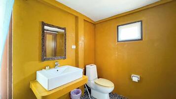 A bathroom with a yellow wall, a white sink, a toilet, and a small window.