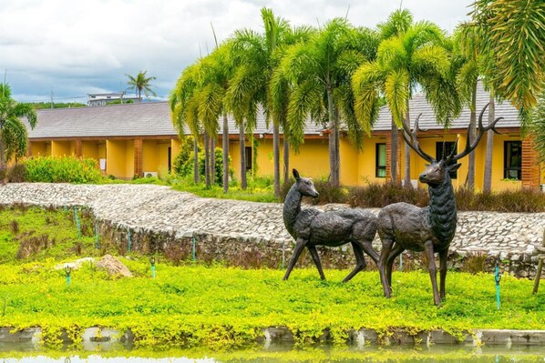 A yellow building with a stone pathway and a statue of two deer in a garden. - Prew Lom Chom Nam (Pluak Daeng)