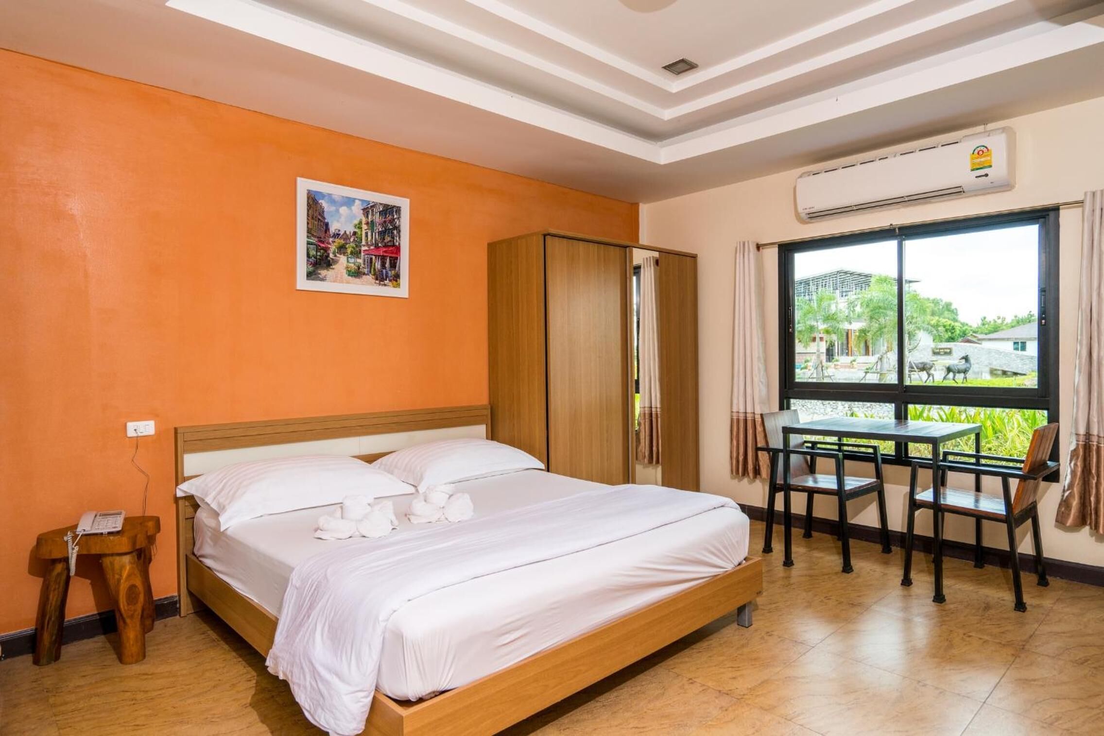 Habitación de hotel con cama, una pequeña mesa con sillas, un equipo de aire acondicionado y una ventana con vistas a zonas verdes.