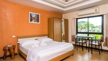Habitación de hotel con cama, una pequeña mesa con sillas, un equipo de aire acondicionado y una ventana con vistas a zonas verdes.