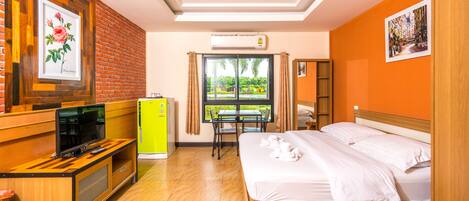 A hotel room with a bed, a desk with a television, a small table, and a window with curtains.