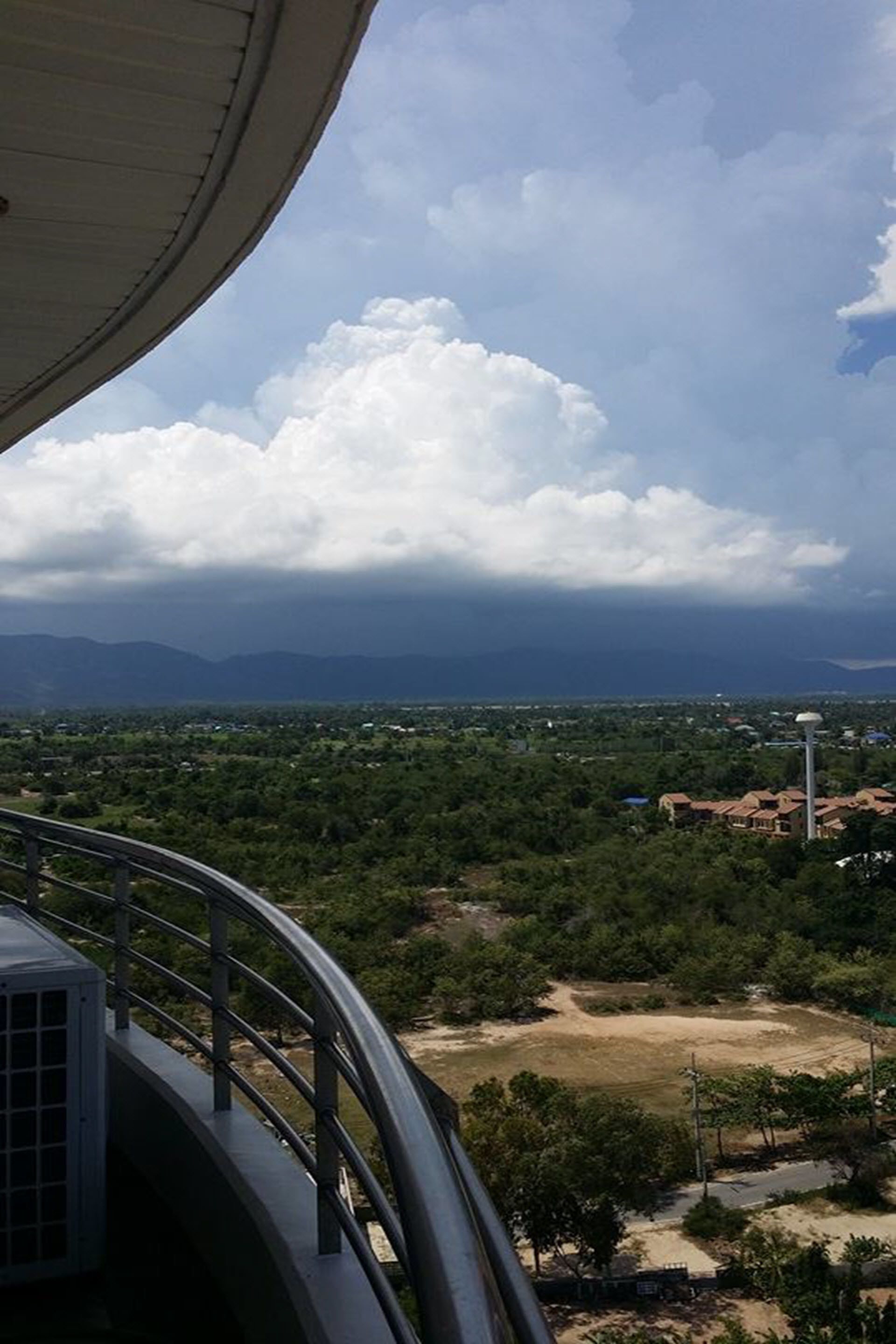 Une vue depuis un balcon doté d’une balustrade, donnant sur un paysage composé d’arbres et de bâtiments.