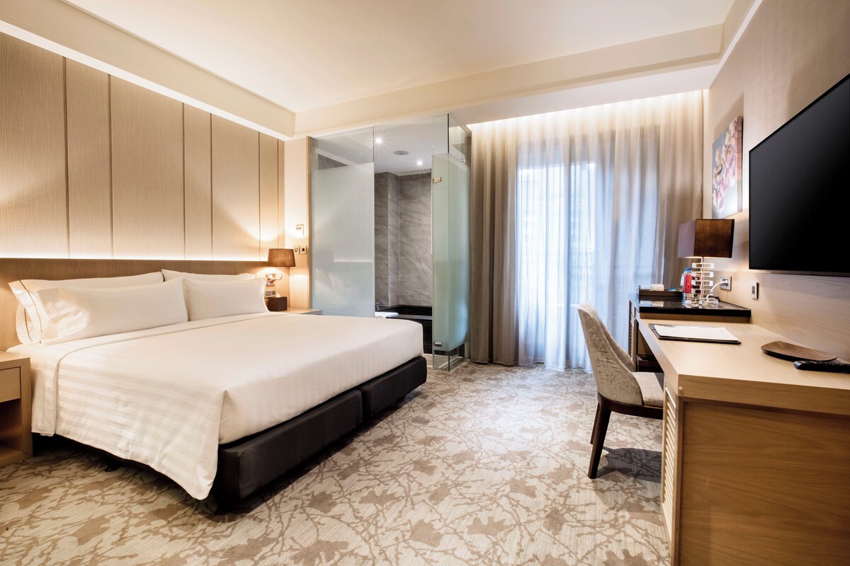 A modern hotel room with a large bed, a desk, and a television.