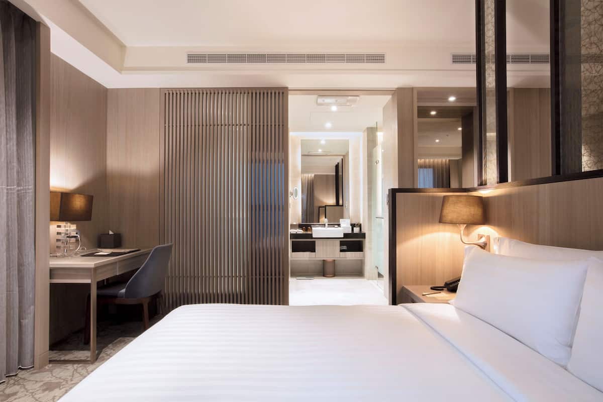 Ein Hotelzimmer mit Bett, Schreibtisch, Stuhl und einem durch eine offene Tür einsehbaren Badezimmer.