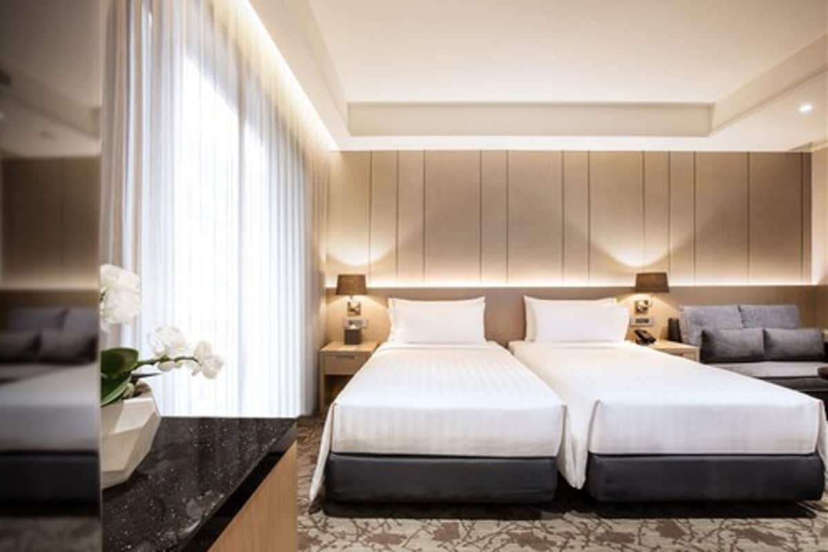 Ein modernes Hotelzimmer mit zwei Betten, einer Marmorplatte im Badezimmer und einem großen Fenster mit Vorhängen.