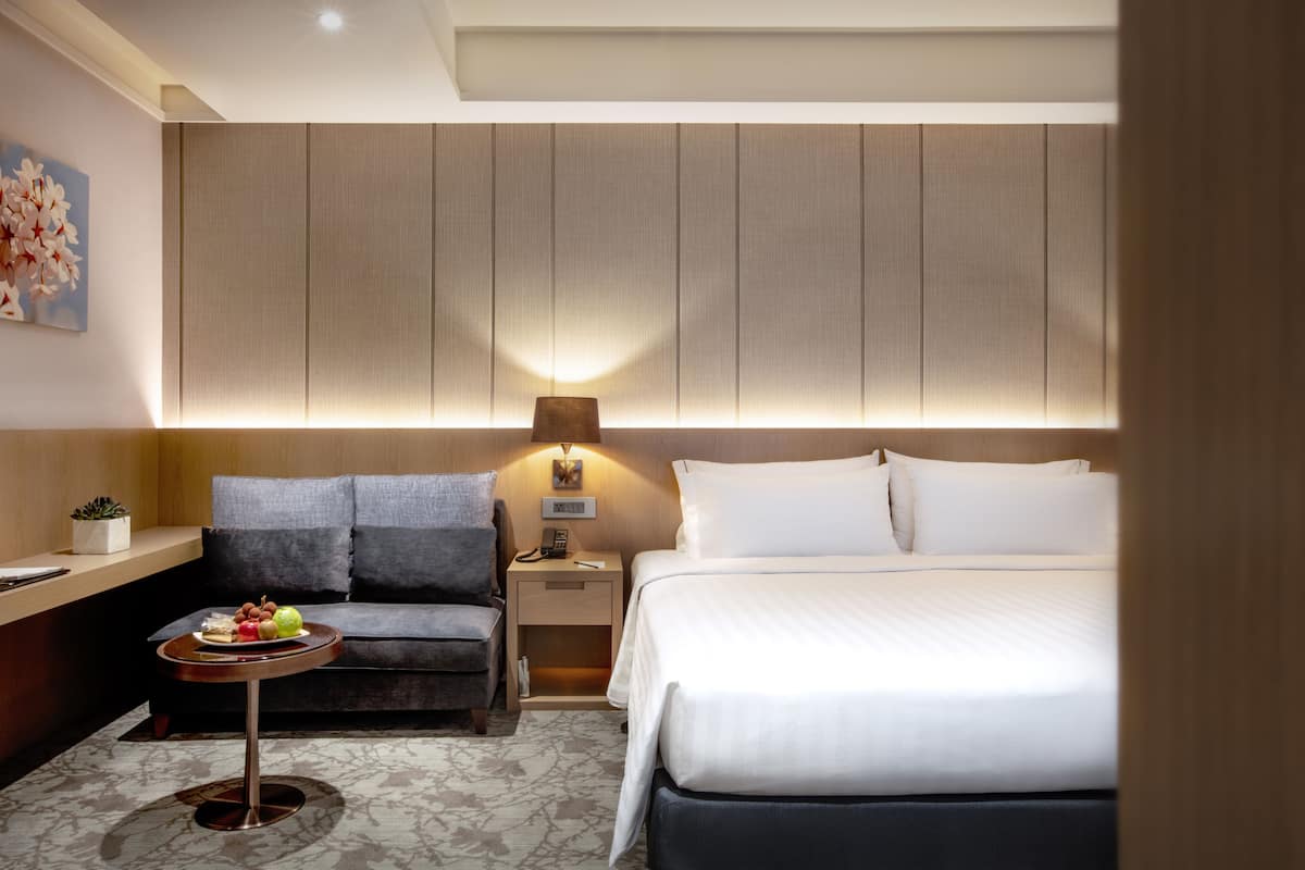 Ein Hotelzimmer mit einem Bett, einer Couch, einem kleinen Tisch mit Lampe und einem Nachttisch.