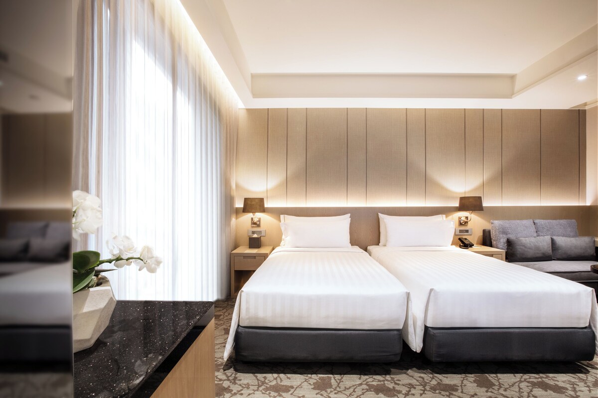 A modern hotel room with two beds, a marble countertop, and a large window with curtains.