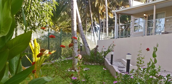 A garden area with a fence, palm trees, and a building with a balcony.