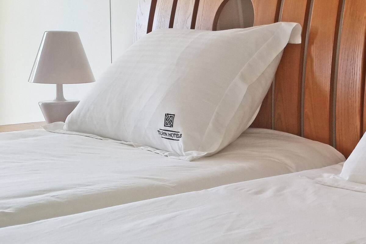 Habitación de hotel con dos camas, cada una con un almohadón que muestra el logotipo de 'Turin Hotels'.