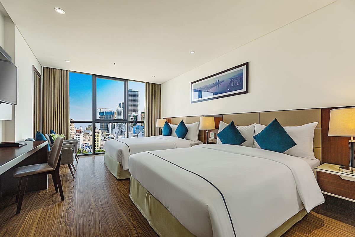 Quarto de hotel com duas camas, uma mesa e uma cadeira.