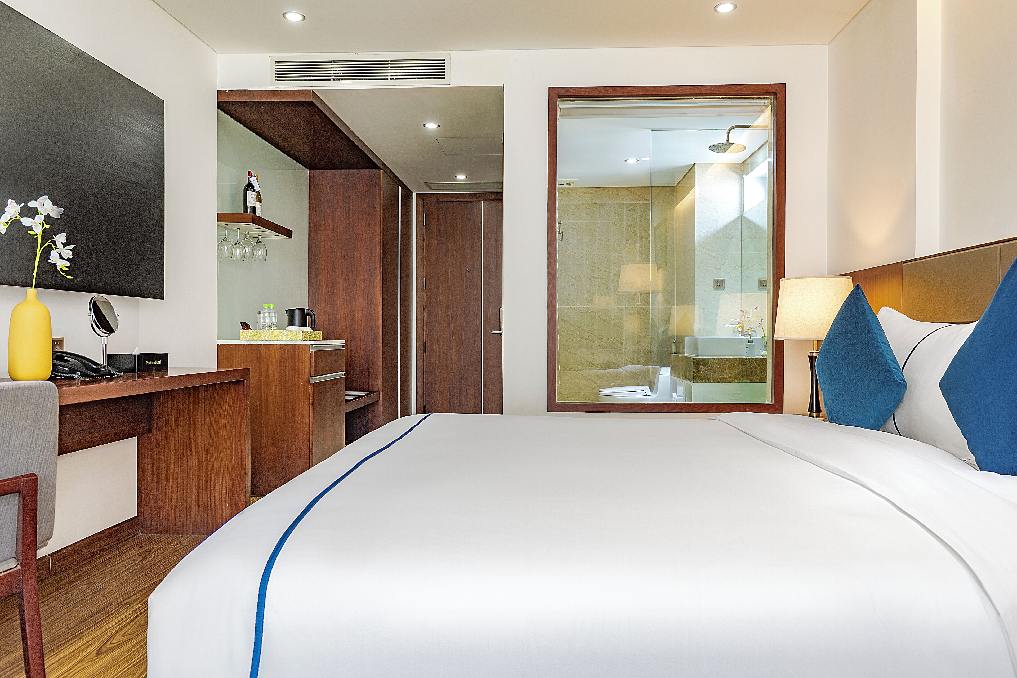 A hotel room with a large bed, a desk with a telephone, a mirror, and a small table with a vase of flowers.