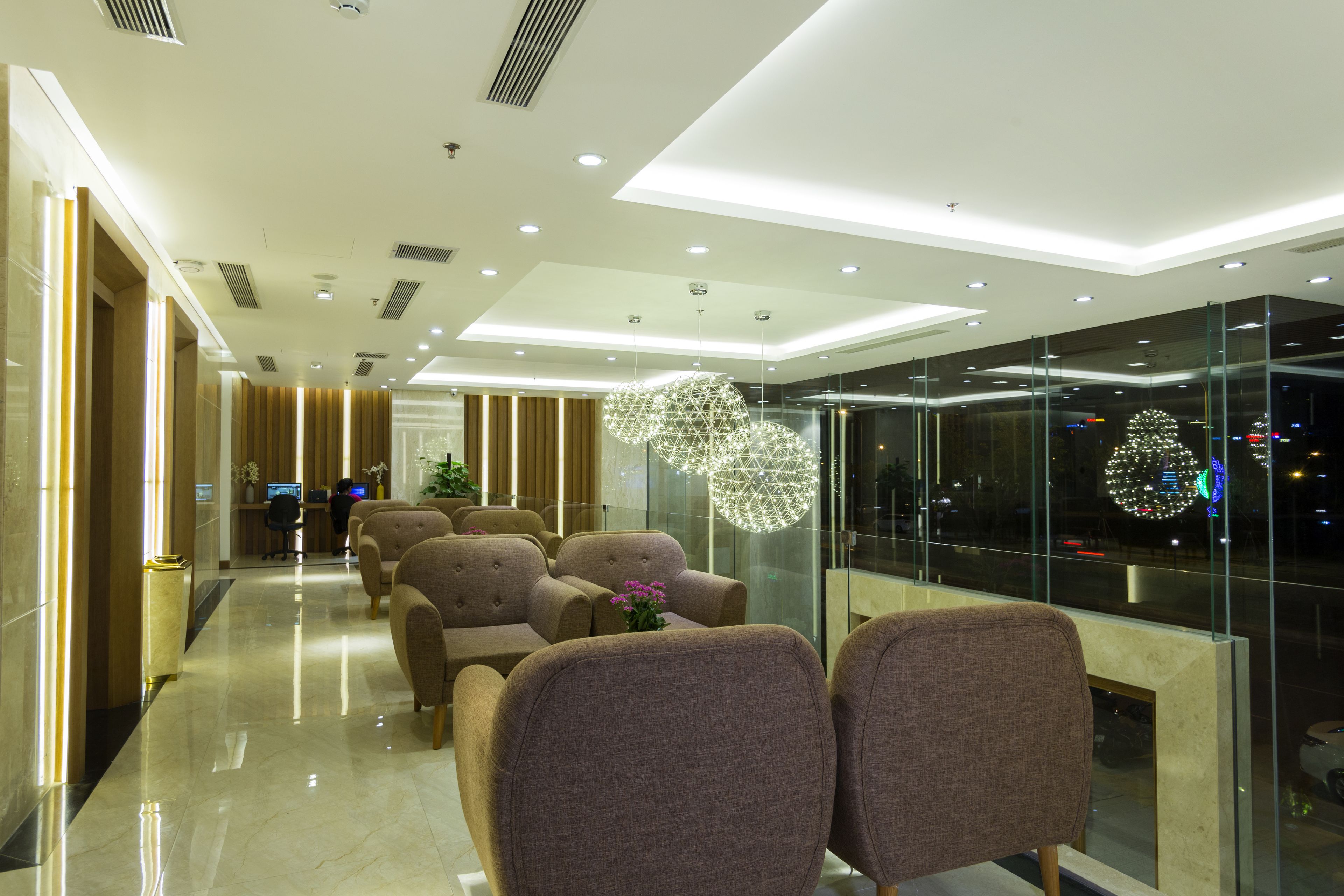 A modern lobby with a glass wall, seating area, and a decorative light fixture.