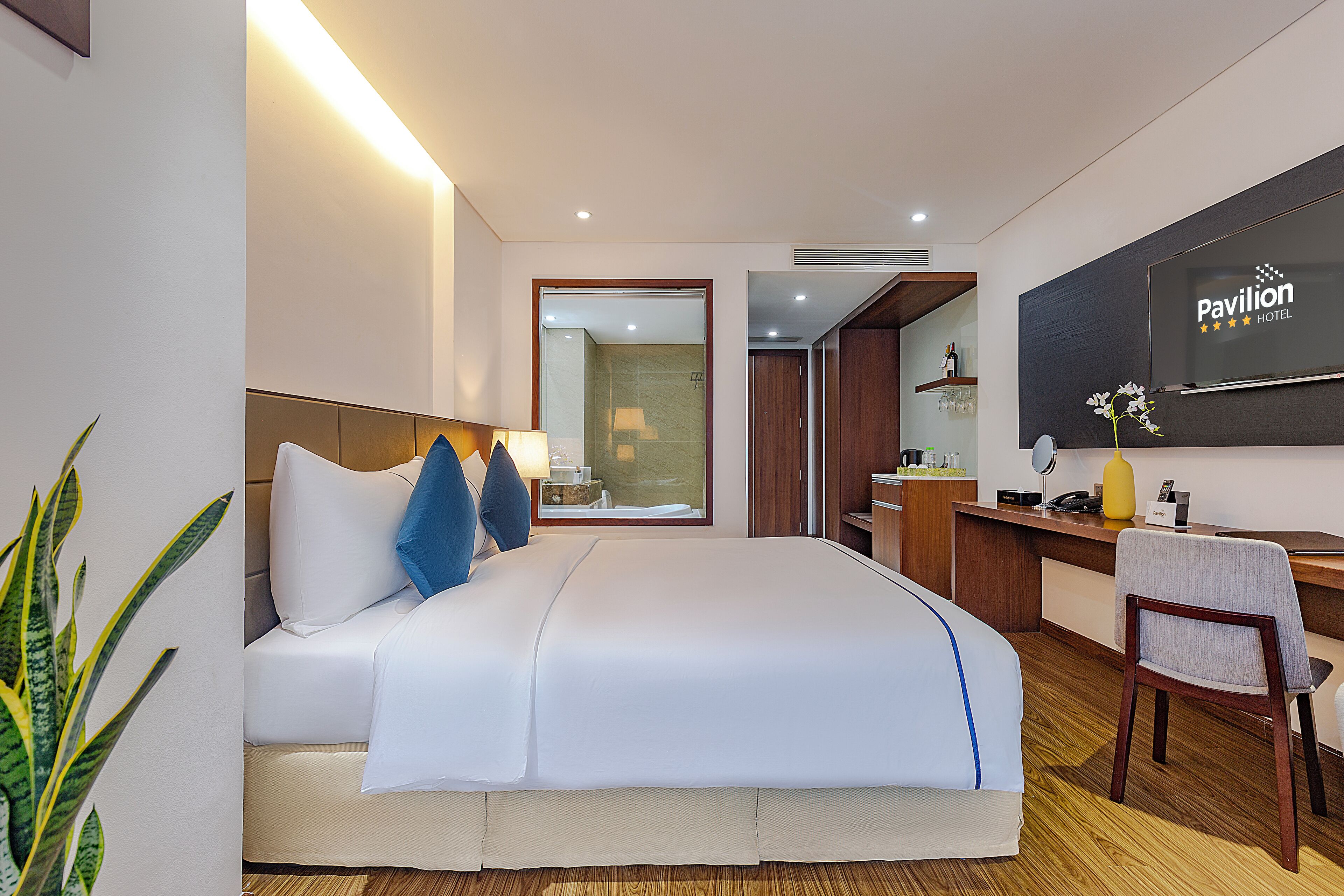 Habitación de hotel con cama, escritorio, silla y televisor mostrando el nombre del hotel.