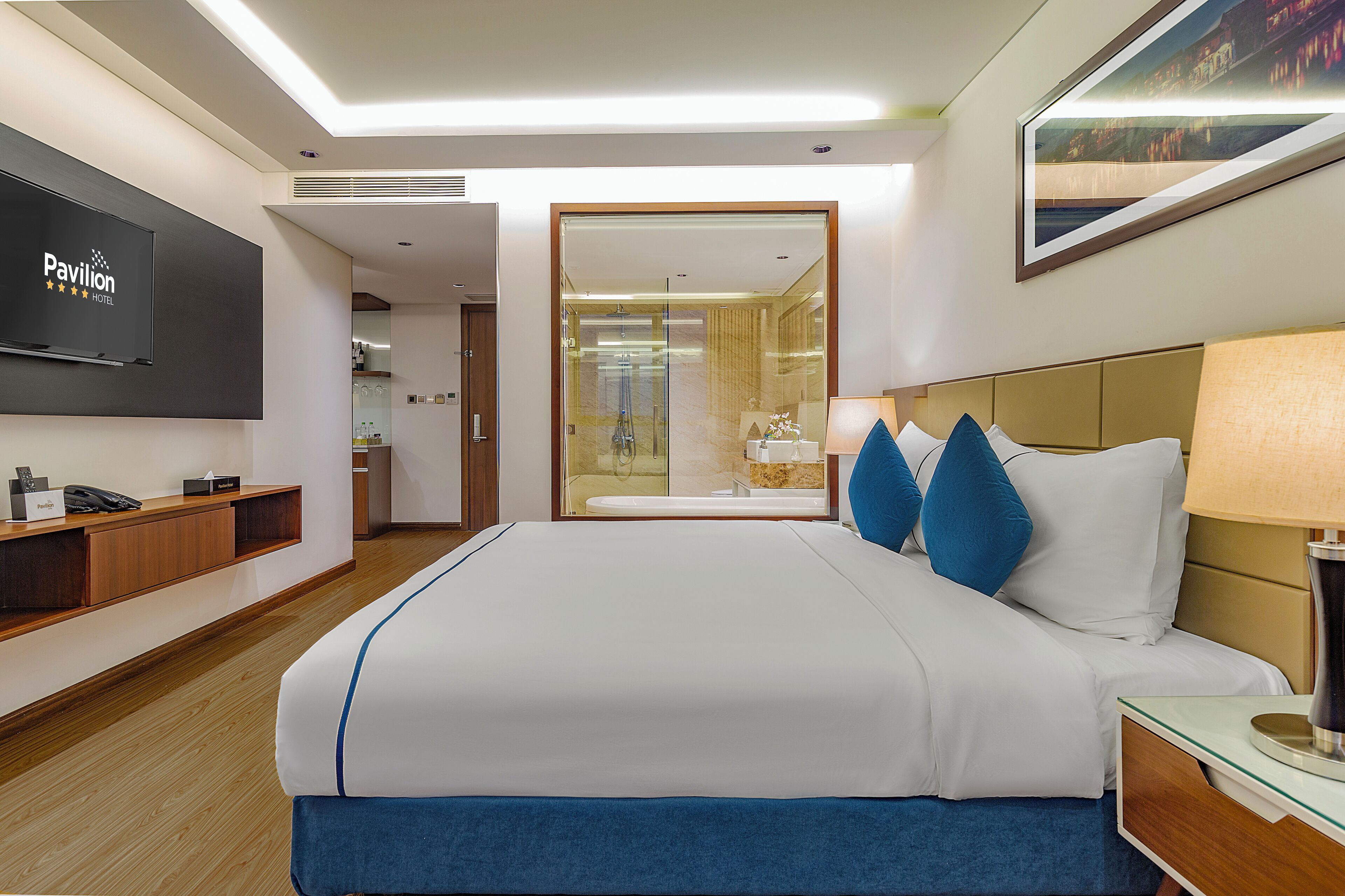 A hotel room with a large bed, a TV mounted on the wall, a bedside table, and a view of the bathroom through a glass door.