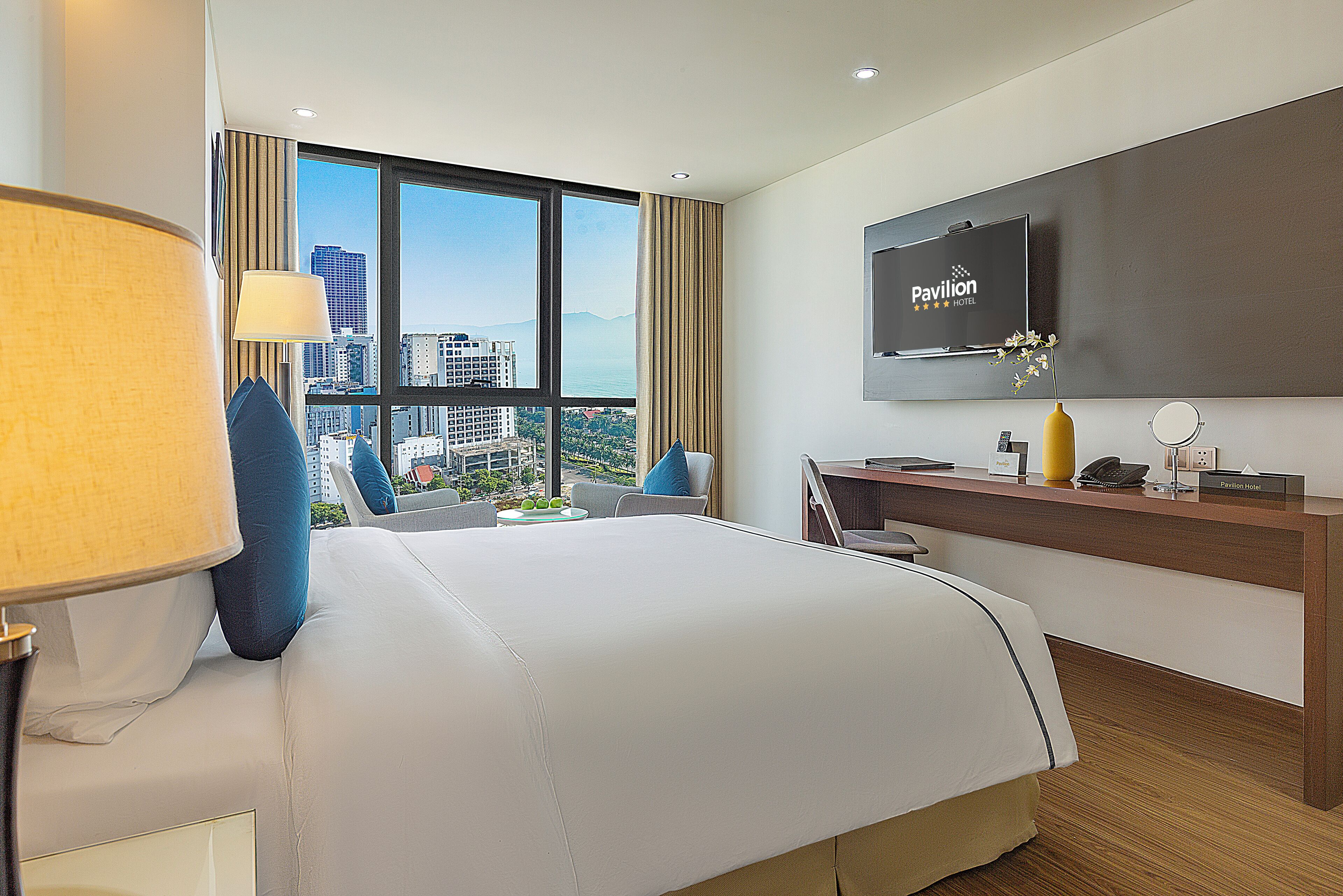 A hotel room with a large bed, a desk, a television, and a view of the city.