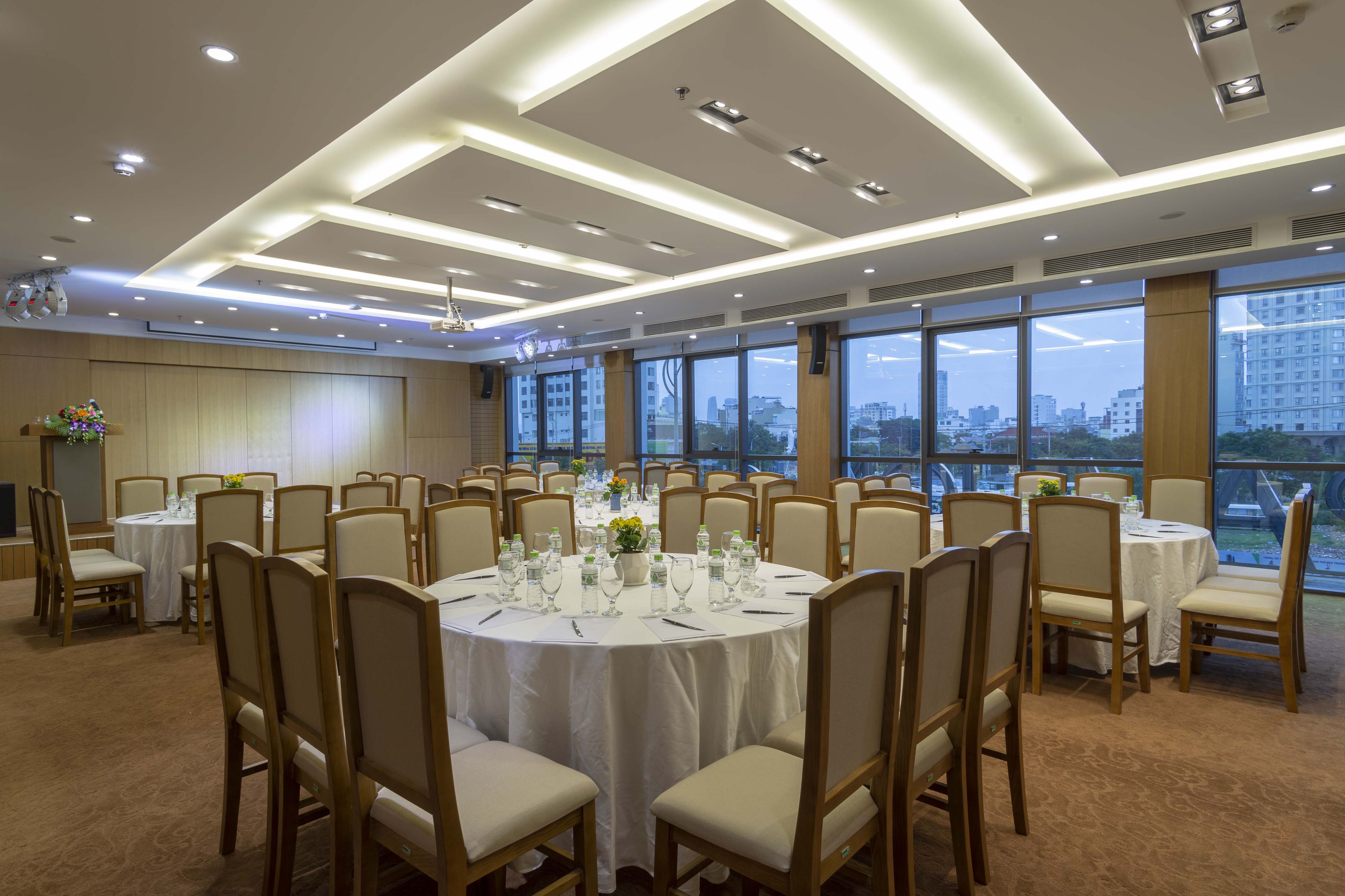Un salón de conferencias con mesas redondas, sillas y vistas a la ciudad a través de amplias ventanas.