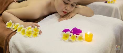 A massage therapy session with a person lying face down on a massage table, another person applying pressure with a tool, and a lit candle on the table.