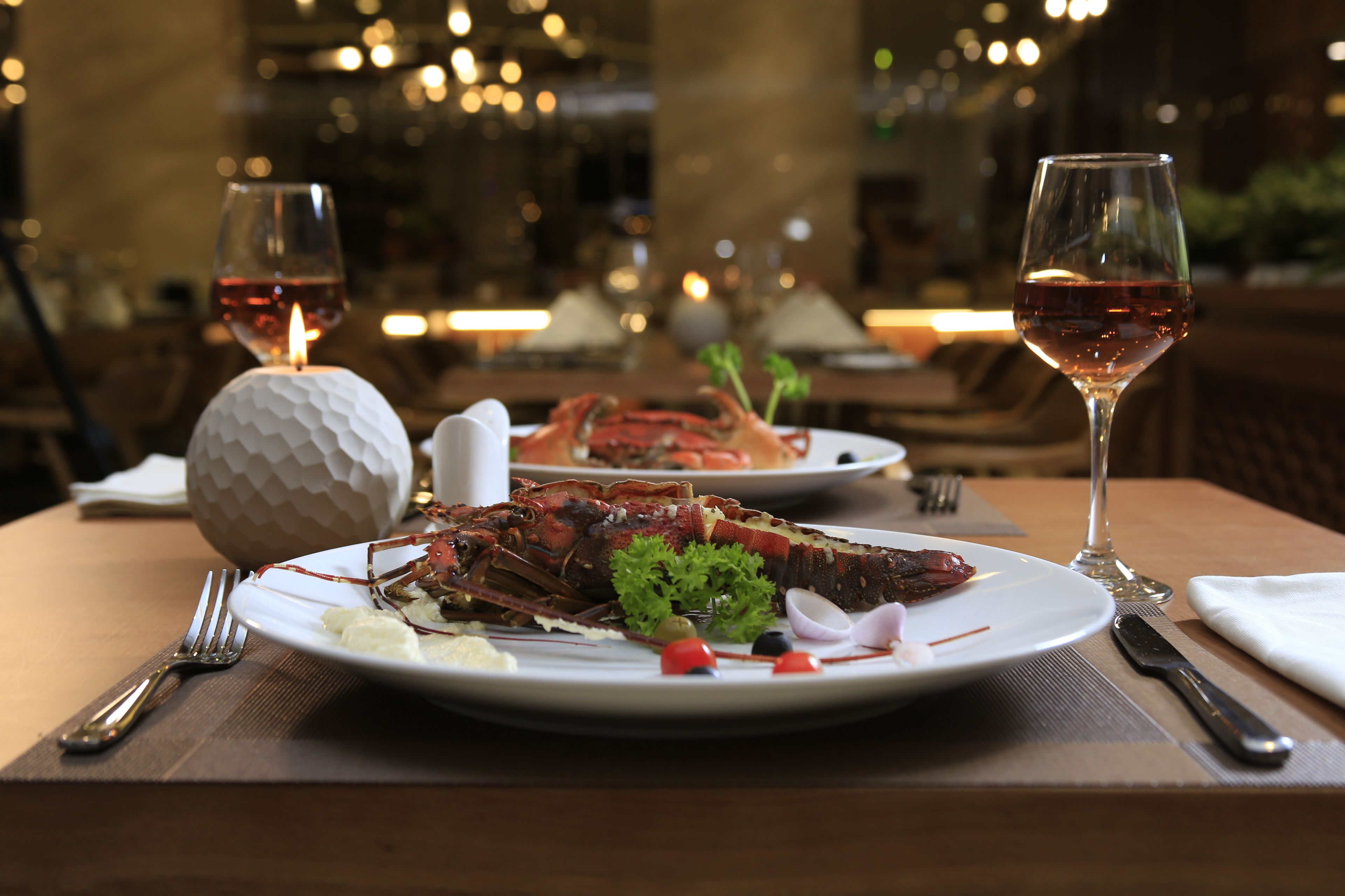 A dining table with a lobster dish, wine glasses, and a candle.