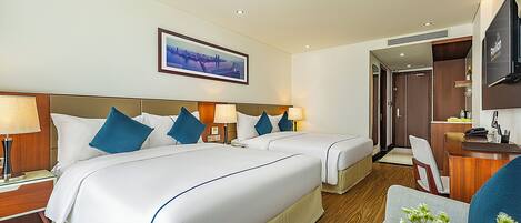 A hotel room with two beds, a desk, a TV, and a framed picture on the wall.