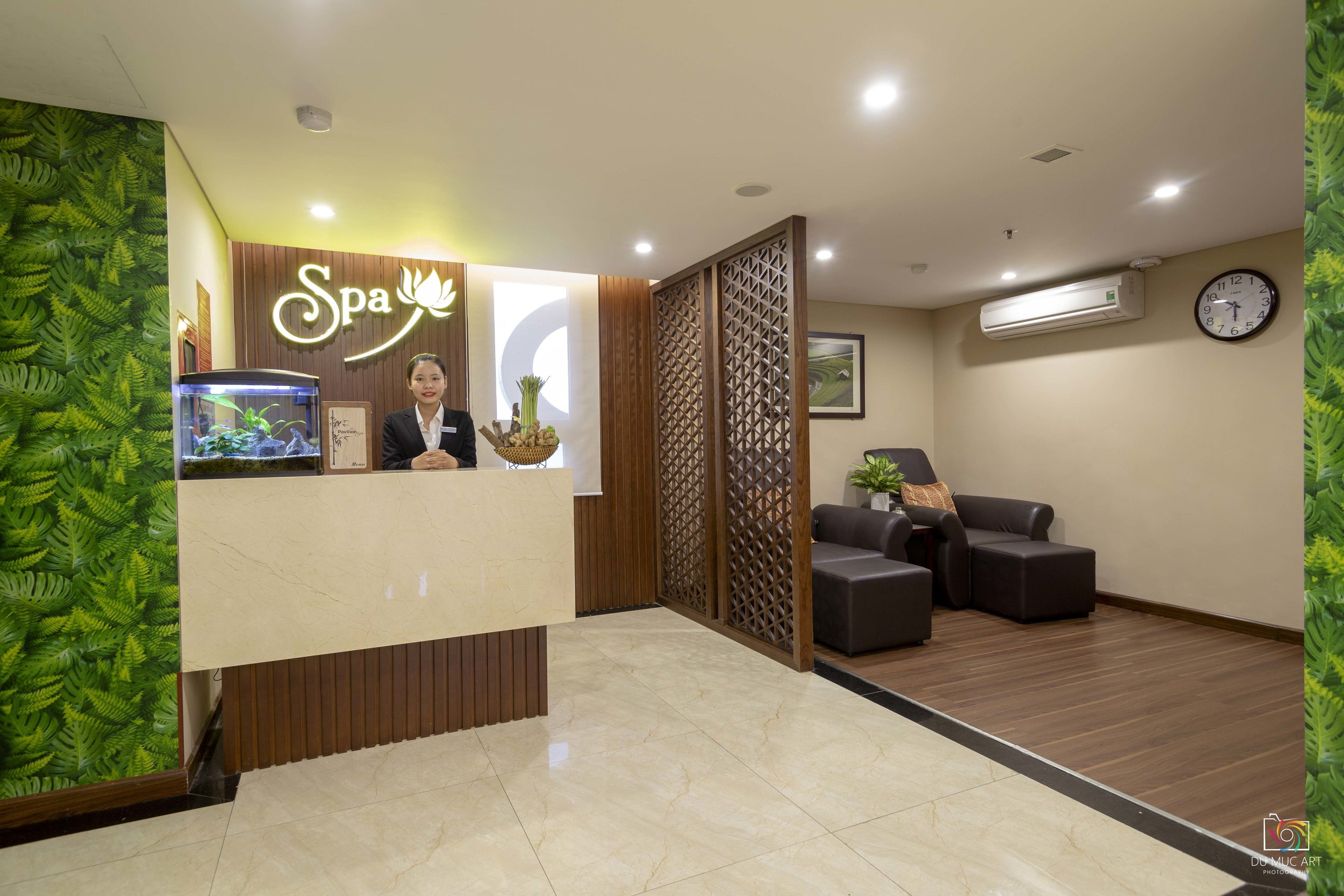 Zona de recepción de spa con mostrador, reloj y área de estar.