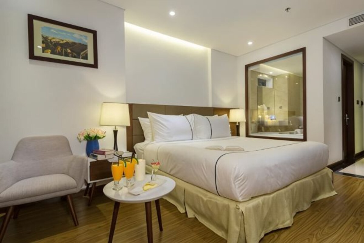 A hotel room with a bed, bedside table, chair, and a large mirror.