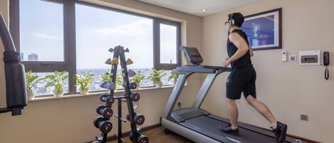 A gym with a treadmill, dumbbells, and a window with a city view.