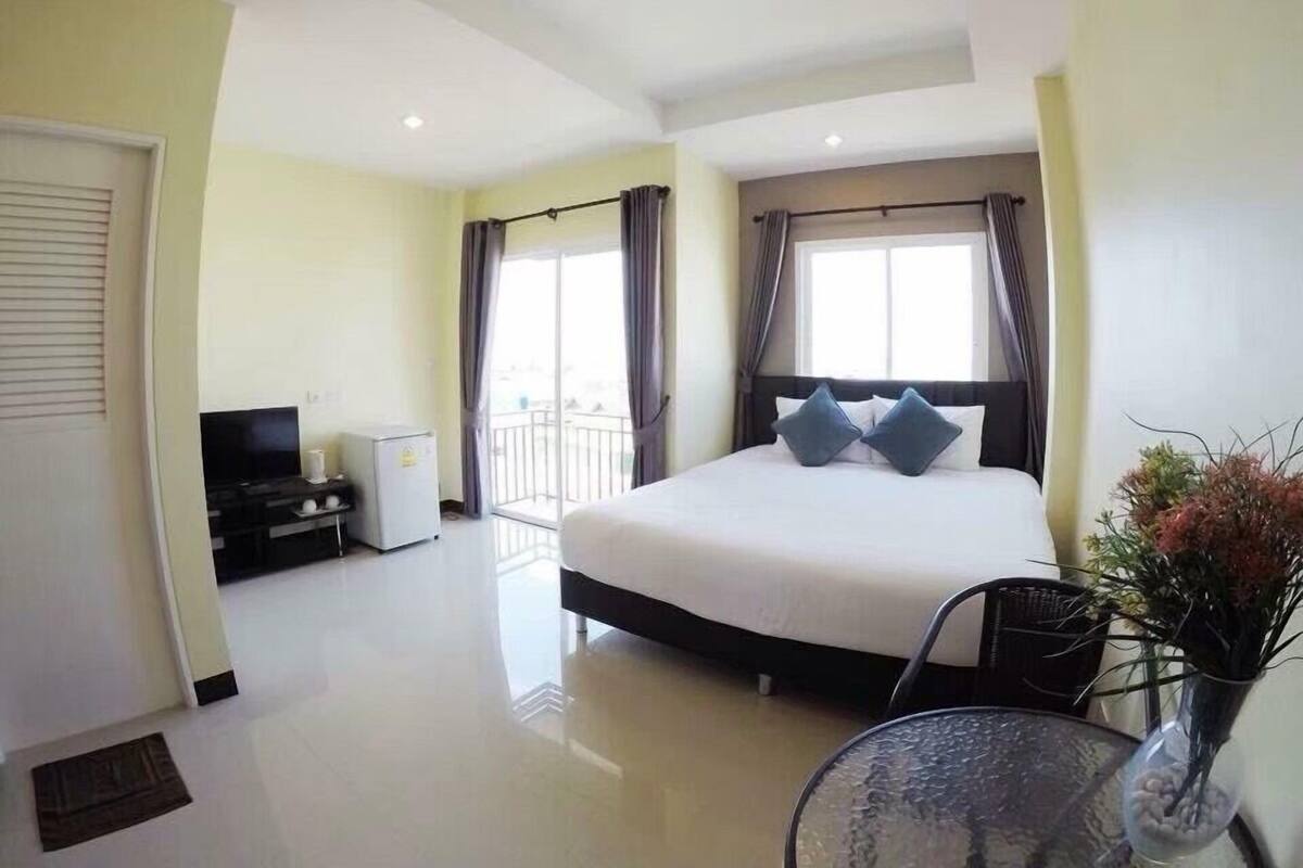 Une chambre d’hôtel avec un grand lit, une télévision, un petit réfrigérateur, un balcon et une table à manger.