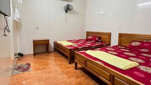 Een kamer met twee houten bedden, een klein nachtkastje van hout, een witte airconditioning en een betegelde vloer.