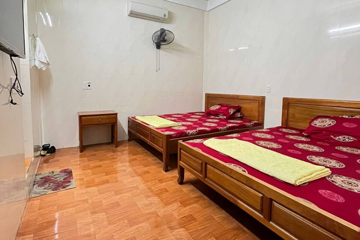 Une chambre avec deux lits en bois, une petite table de chevet en bois, un appareil de climatisation blanc et un sol carrelé.