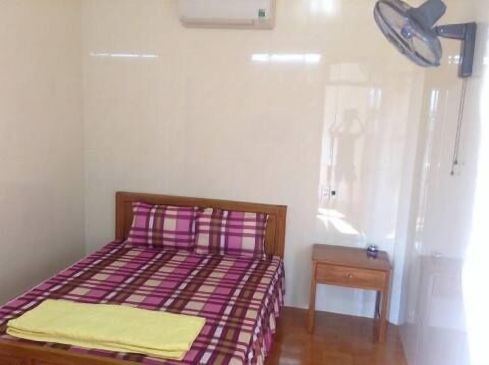 A small, clean room with a bed, a bedside table, and a ceiling fan.