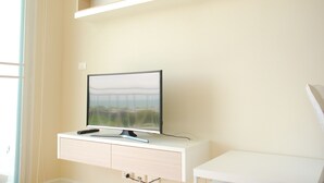 A modern, minimalist room with a mounted TV on a white console, a window, and built-in shelving above the console. - The Legend Boathouse - 904 (Cha-am)