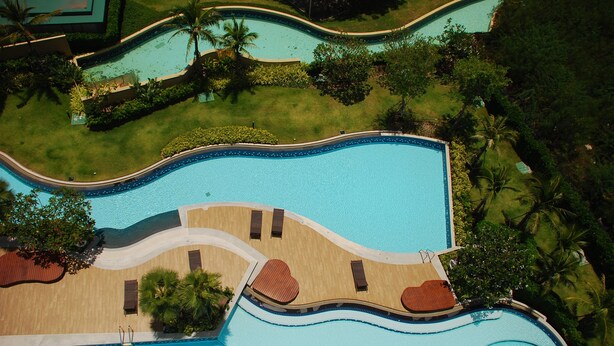 An aerial view of a resort with a large swimming pool, surrounded by palm trees and greenery. - The Legend Boathouse - 904 (Cha-am)