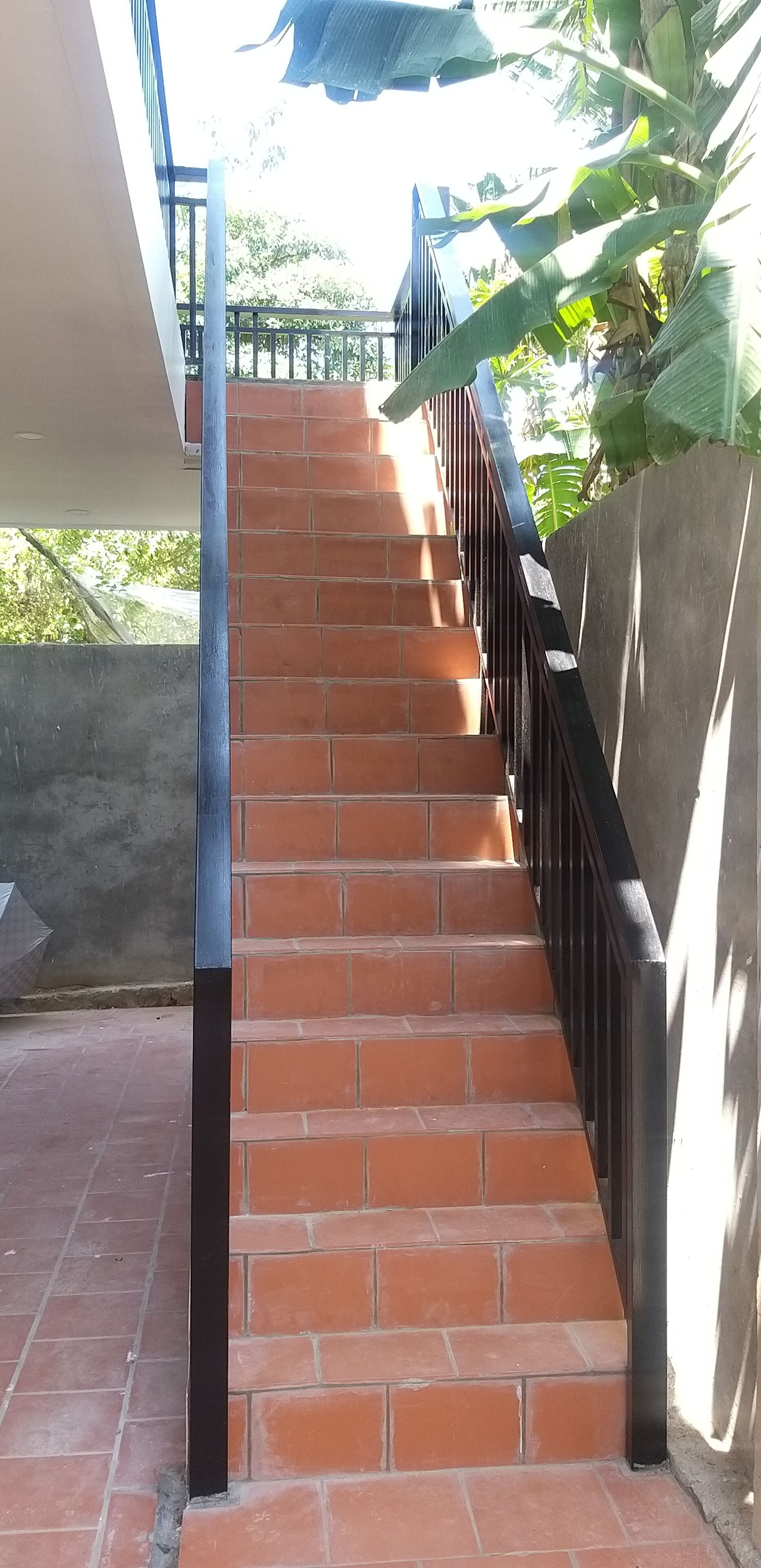 Escadaria com azulejos vermelhos e guarda-corpos pretos, levando a um andar superior.