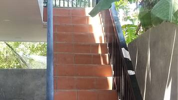 Escadaria com azulejos vermelhos e guarda-corpos pretos, levando a um andar superior.