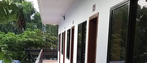 Un pasillo con suelo de baldosas, paredes blancas y ventanas grandes.