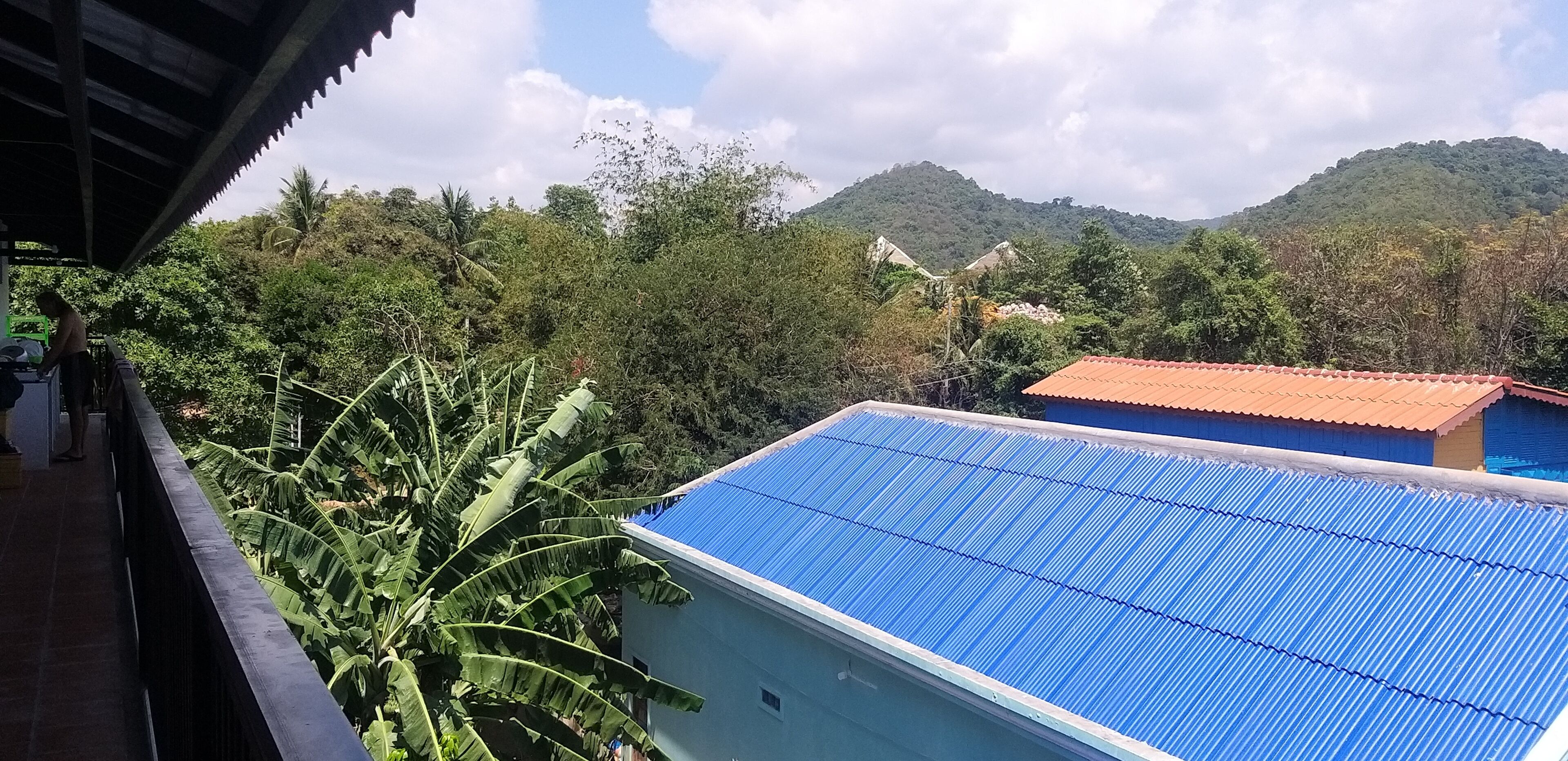 A building with a blue roof, surrounded by lush greenery and hills in the background.