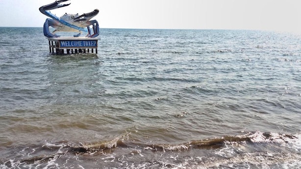 Een strand met een grote krabbeeldhouwing op een pier, en de oceaan op de achtergrond.