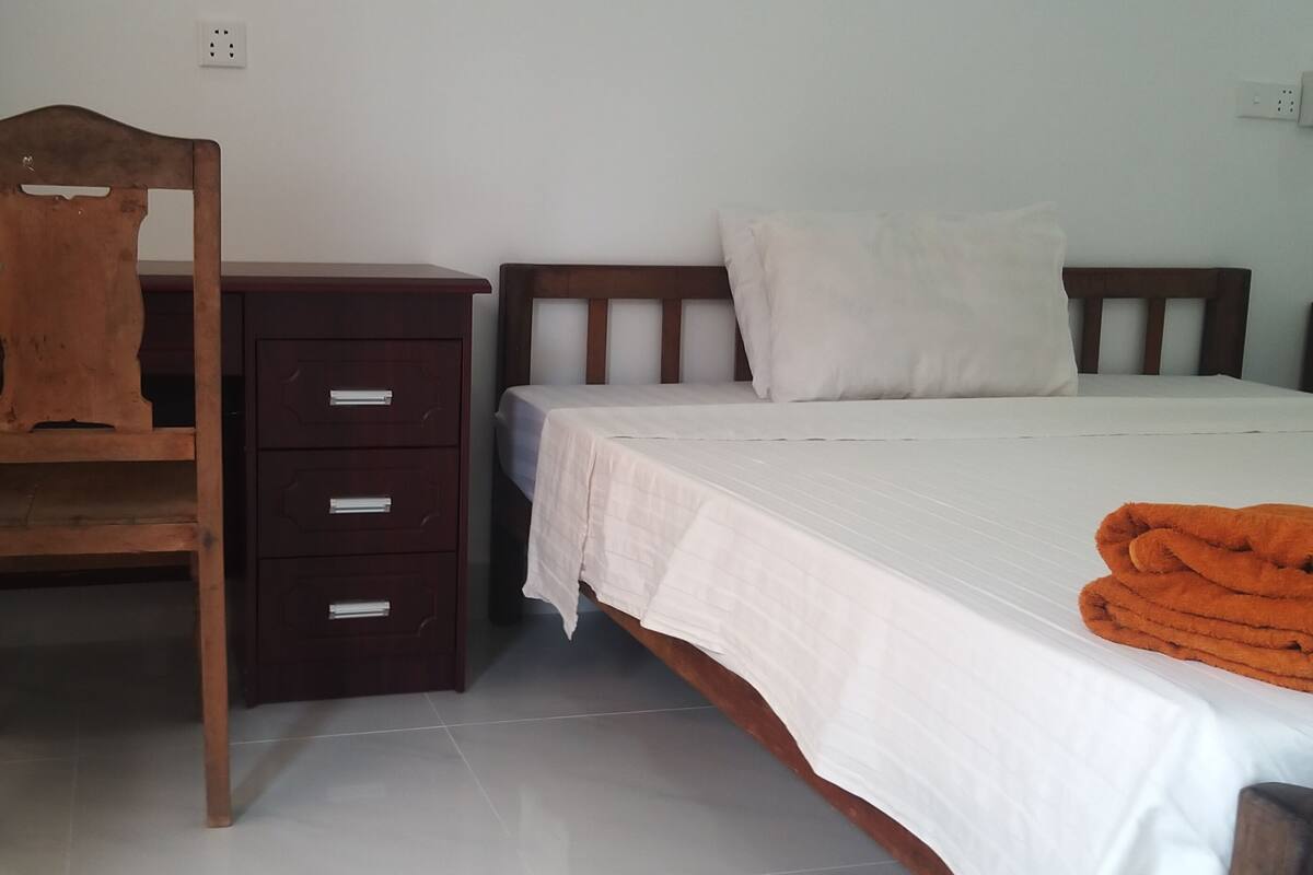 A bedroom with a bed, a wooden chair, a desk, and a dresser.