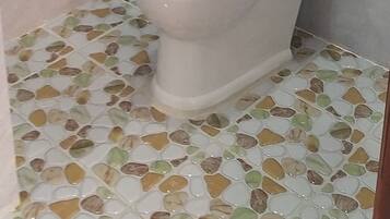A bathroom with a toilet, a paper towel dispenser, and a tiled floor.