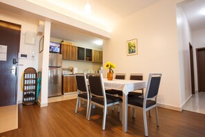 A modern kitchen with stainless steel appliances, a dining area with a white table and chairs, and a wooden floor.