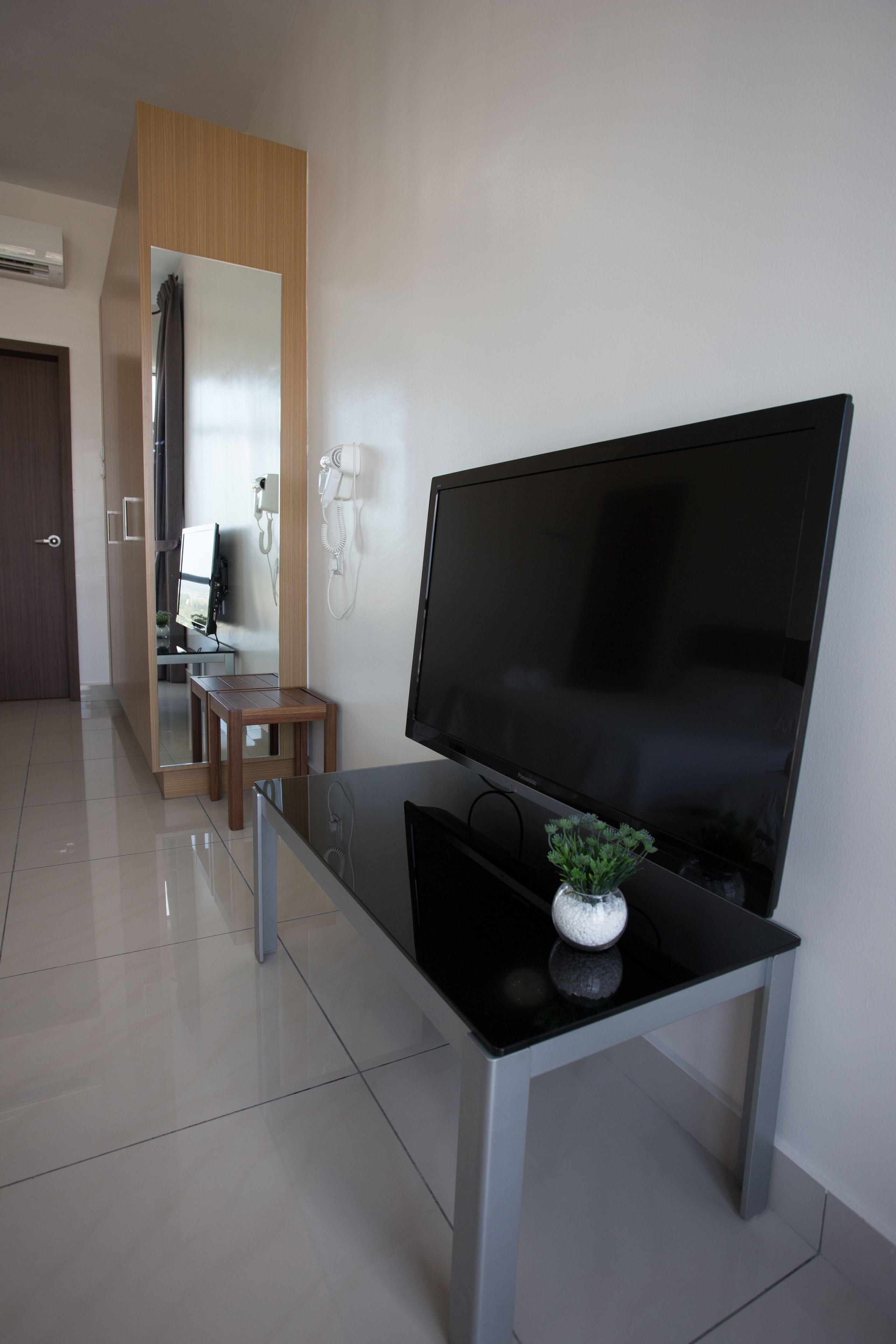 A modern living room with a large flat-screen TV on a glass table, a small wooden side table, and a potted plant.