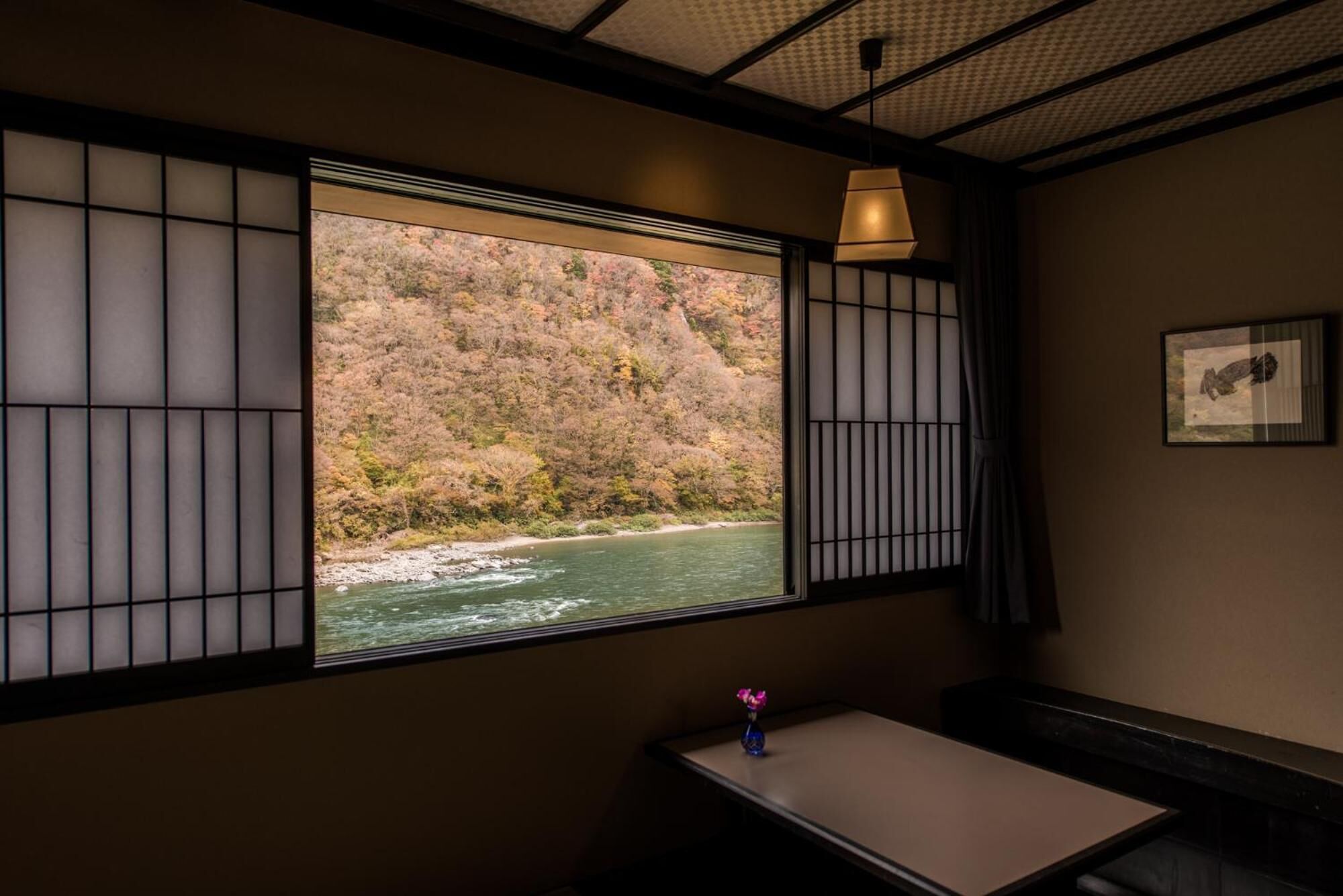 Une pièce avec vue sur une rivière et des collines, une petite table avec un vase et une lampe.