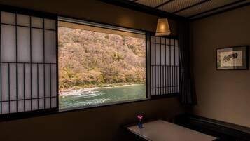 Une pièce avec vue sur une rivière et des collines, une petite table avec un vase et une lampe.
