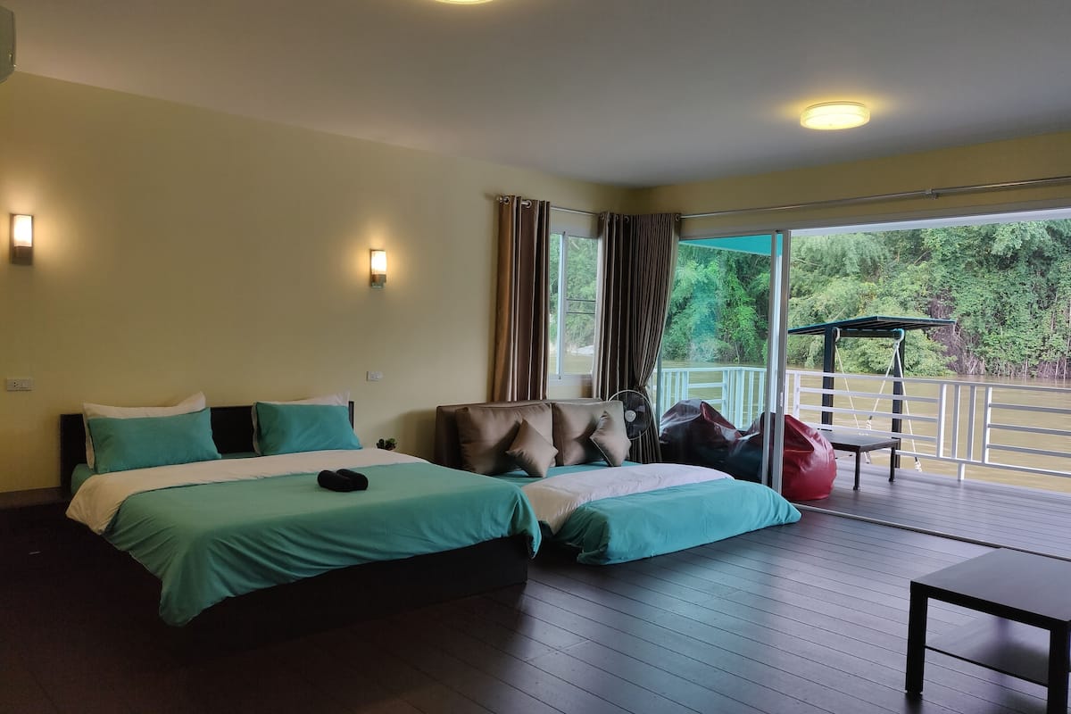Een hotelkamer met twee bedden, een balkon met uitzicht op een rivier en een tafel.