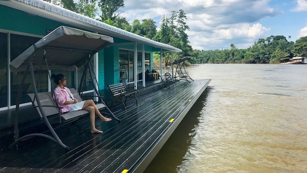 Un bote con cubierta, una persona sentada en un banco y un río tranquilo al fondo.