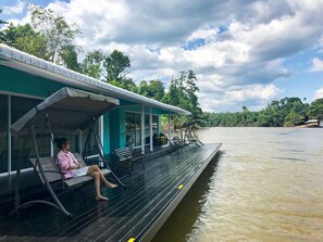 Ein Boot mit überdachtem Deck, eine Person sitzt auf einer Bank und im Hintergrund fließt ein ruhiger Fluss.