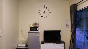 Una habitación con un reloj de pared, microondas, refrigerador, televisor y ventana con cortinas.