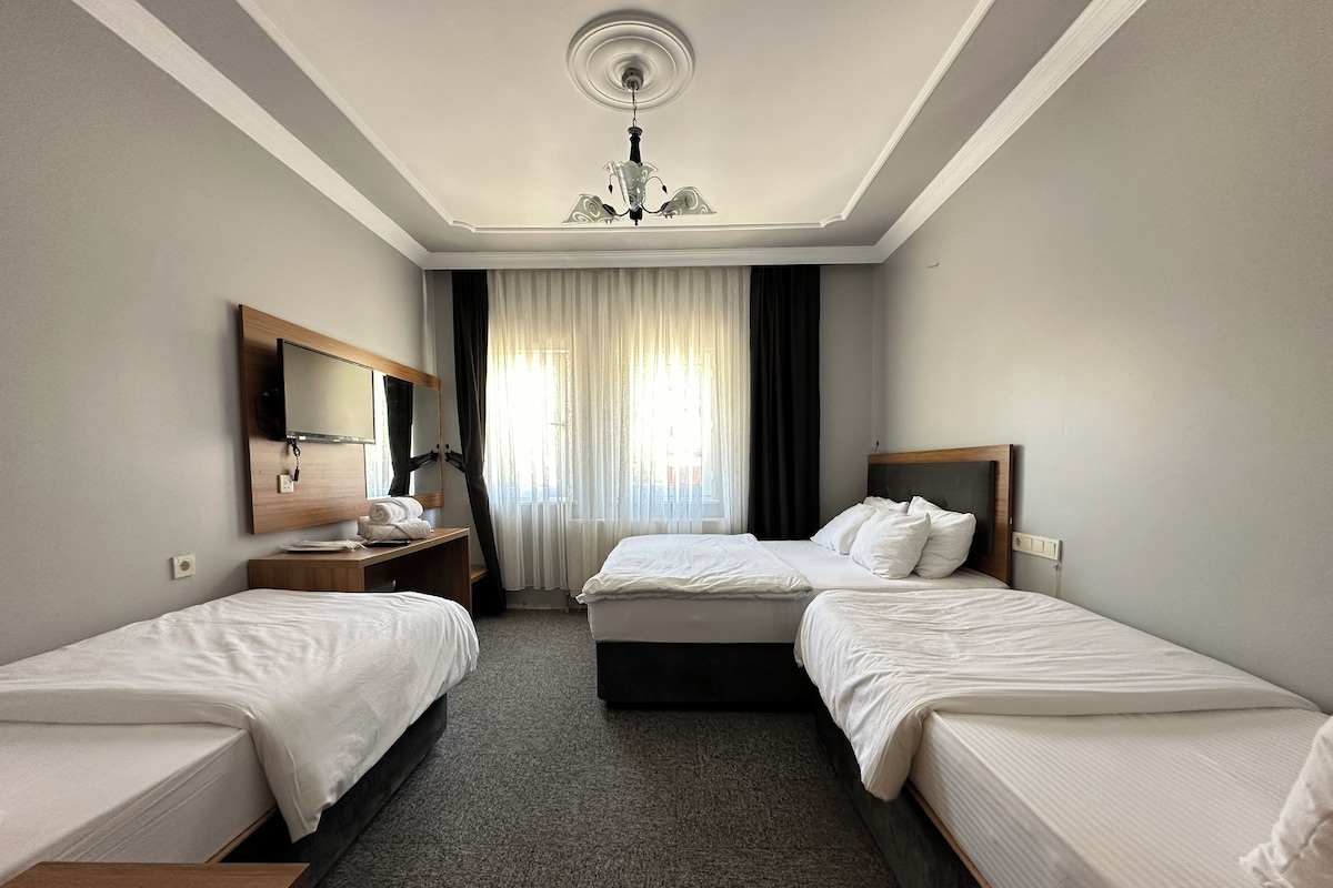 A hotel room with two single beds, a wooden desk, a mirror, a chandelier, and a window with curtains.