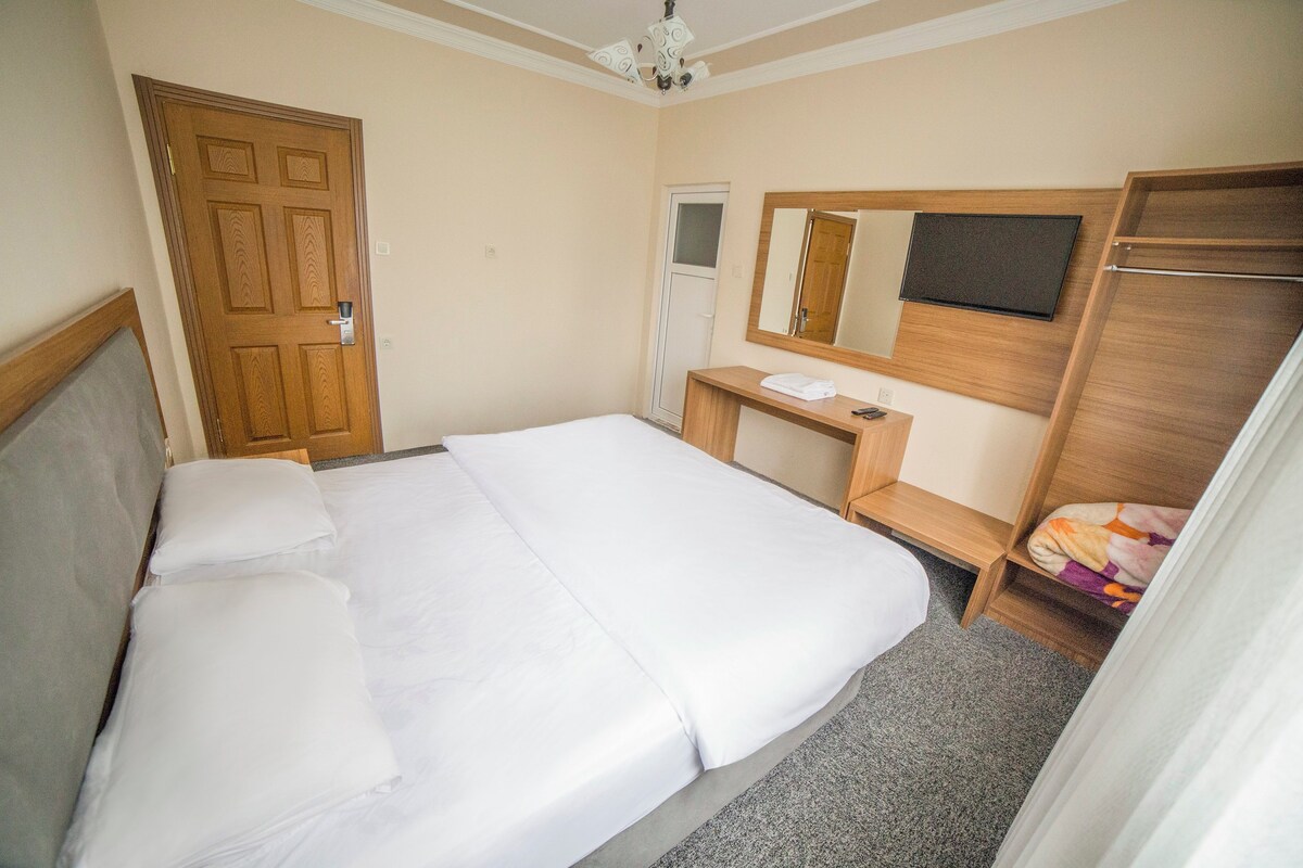 A hotel room with a bed, a desk, a mirror, and a wardrobe.