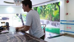A man cleaning a marble countertop in a modern hotel lobby with a waterfall mural and a ceiling light fixture. - Yen Vy 32 Hotel - Hostel (Quy Nhon Nam)